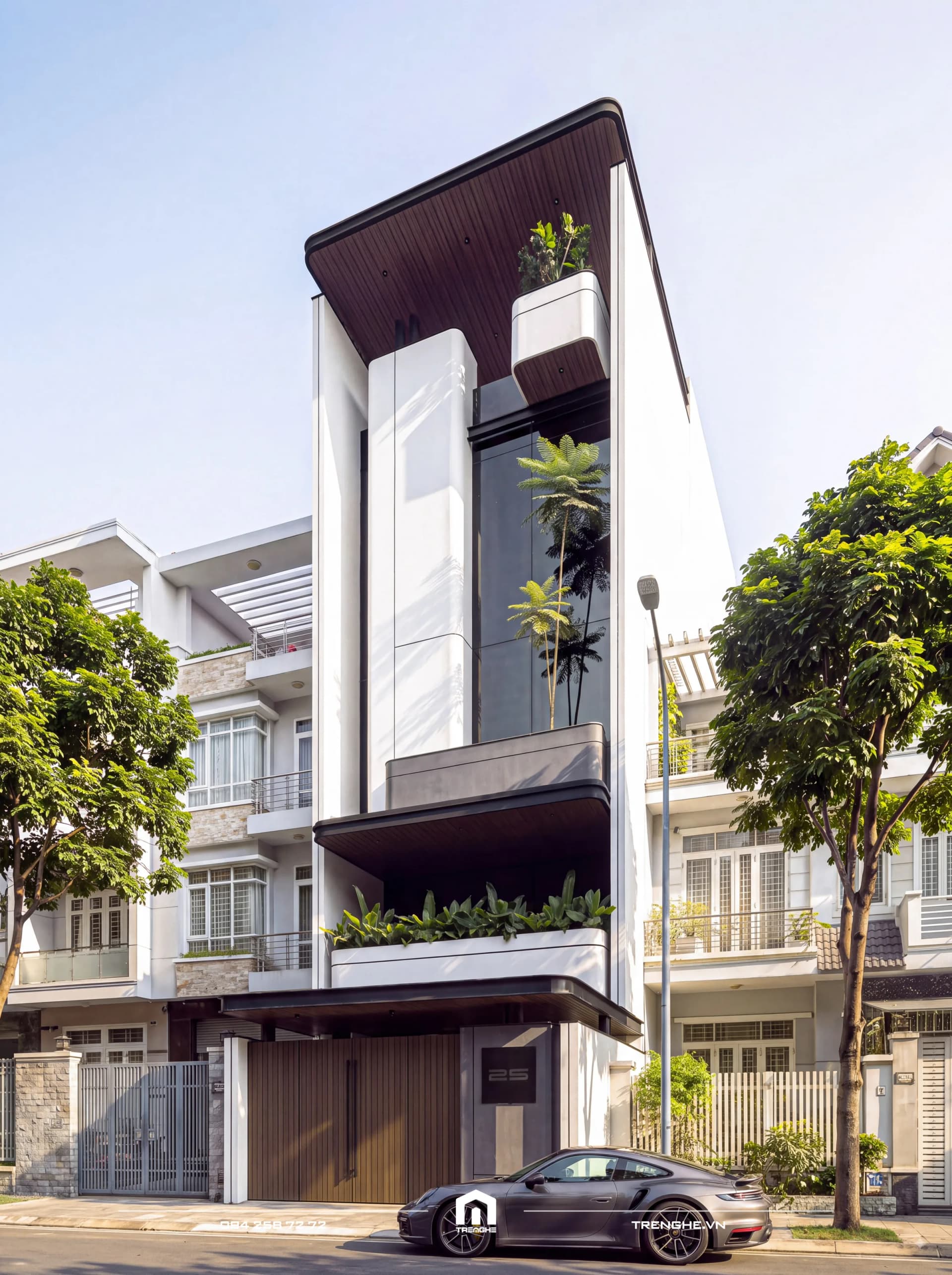 Mặt tiền nhà phố hiện đại H’ House ban ngày: khối trắng bo cong, ban công bồn cây, khoảng kính cao trồng cau, mái che ốp nhôm giả gỗ và cổng gỗ số 25