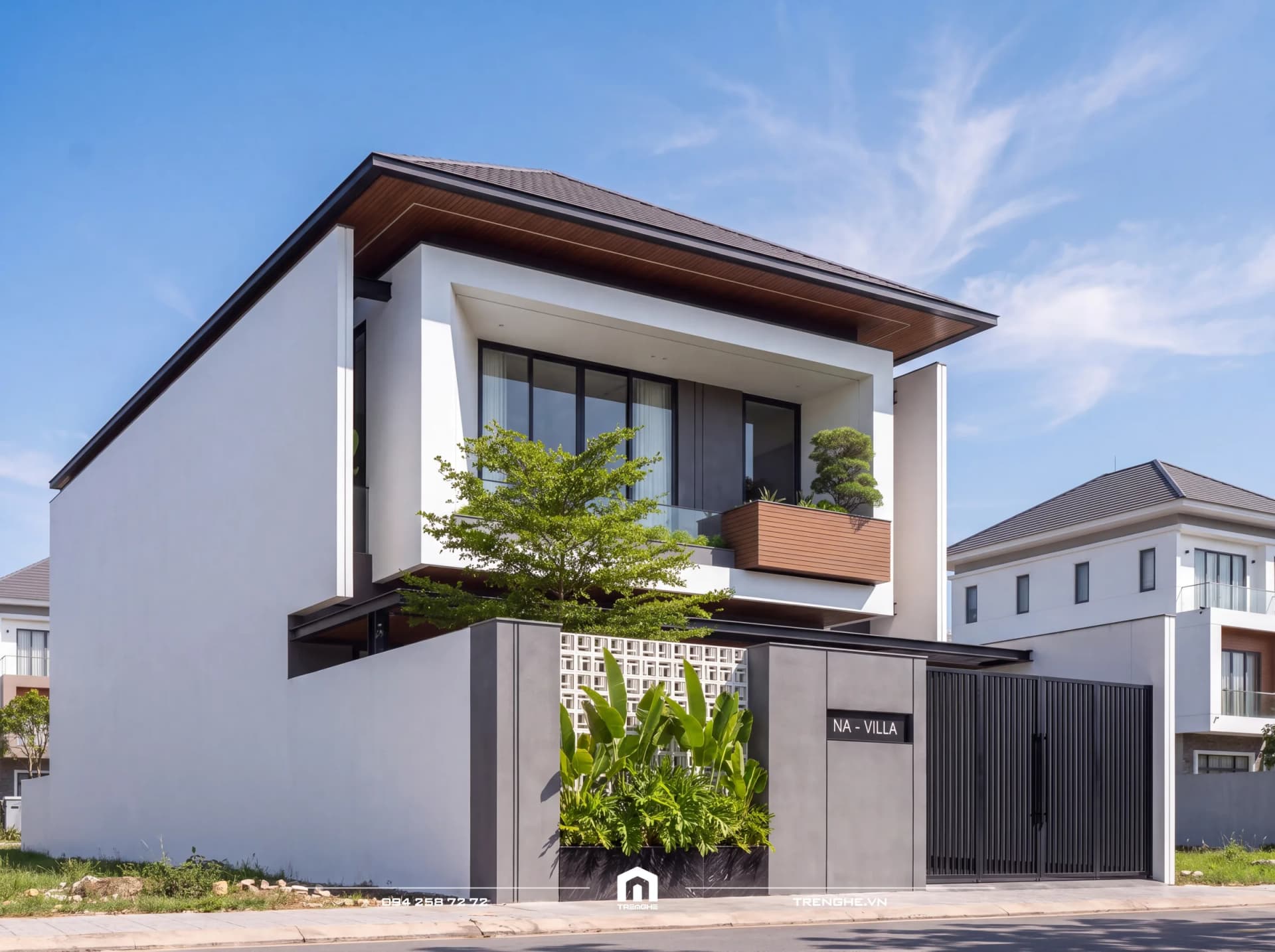 Biệt thự mái Nhật NA’ Villa ban ngày nhìn từ góc trái: mái ngói xám vươn rộng, trần gỗ, khung tường trắng ôm cửa kính lớn, bồn cây bonsai và tường gạch bông gió