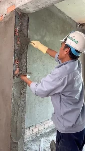 Thợ thi công gạt lớp vừa thừa để tường gọn gàng và đồng đều