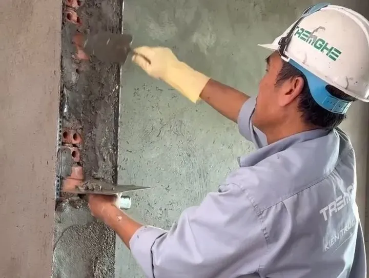 Thợ thi công gạt lớp vừa thừa để tường gọn gàng và đồng đều